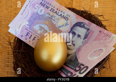 Neuseeland-Dollar und ein goldenes Ei in einem Nest. Stockfoto