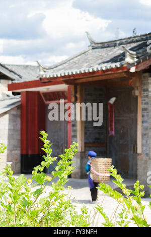 Lijiang, China - 4. Oktober 2014: alte Frau trägt Korb vor traditionellen chinesischen Architektur in Shuhe, Lijiang Altstadt Stockfoto