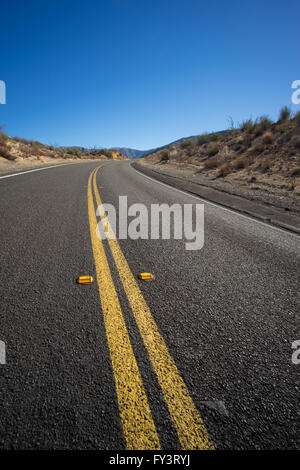 Doppelte gelbe Linie durch die Szene führt von der Autobahn in die Weite der Wüste. Stockfoto