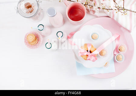 Milchshakes, drei mit einem Strohhalm, vier Flaschen Glas voller Süßigkeiten, rosa Tasse und Glas Milch und Teller mit Keksen Stockfoto