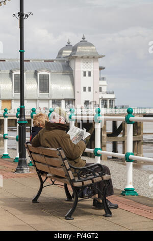 Ein älteres Ehepaar sitzt auf einer Bank und liest eine Zeitung in Penarth Pier. Stockfoto