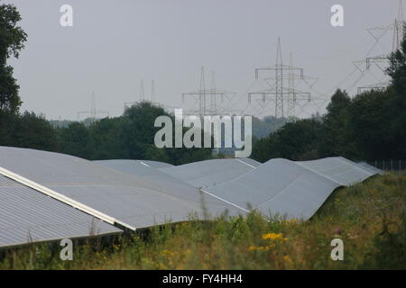 PV-Anlage außerhalb der Stadt mit Stromleitungen im Hintergrund. Stockfoto