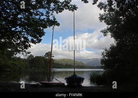 zwei Segelboote vor Anker am Ufer des Lake Windermere, in Cumbria Seenplatte, werfen eine Silhouette unter den Bäumen Stockfoto