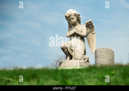 Betender Engelsstatue mit Grabstein im Hintergrund am Friedhof Stockfoto