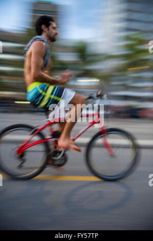 RIO DE JANEIRO - 6. März 2016: Ein junger brasilianischen Mann reitet sein Fahrrad in Bewegungsunschärfe Ipanema Beach direkt am Strand unterwegs. Stockfoto