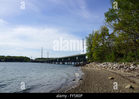 Felsiger Strand führt zu einer Brücke und Stromleitungen Kreuz Wasserstraße verbindet Cousins-Insel mit dem Festland von Maine. Stockfoto