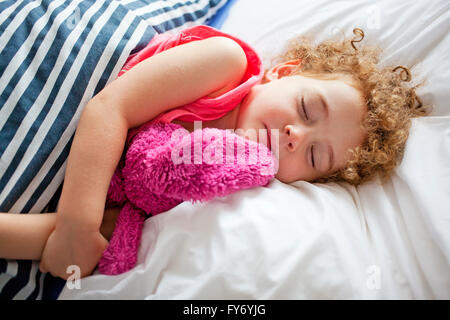 Lockige dunkelhaarige Mädchen schläft mit rosa bunny Stockfoto