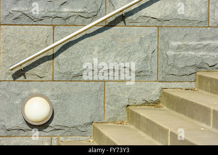 Große Granit-Steinblöcke an einer massiven Wand. Kleine Lampe an der Wand und Treppe nach oben oder unten davor. Stahlgeländer atta Stockfoto