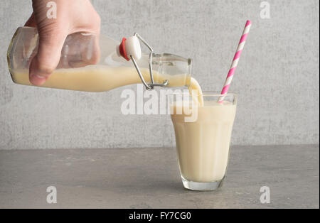 Soja-Milch aus der Flasche in ein Trinkglas mit einem gestreiften Strohhalm gegossen wird. Stockfoto