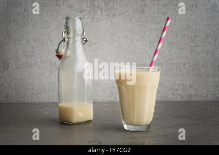 Soja-Milch in ein Glas mit gestreiften trinken Stroh und Glasflasche am Steintisch. Stockfoto