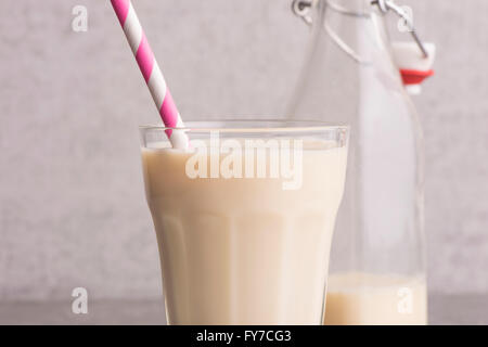 Soja-Milch in ein Glas mit gestreiften trinken Stroh und Glasflasche am Steintisch. Stockfoto