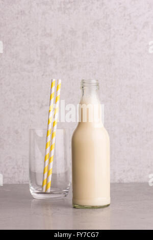 Soja-Milch in einer Glasflasche mit leeren Trinkglas und gestreifte Strohhalme am Steintisch. Stockfoto