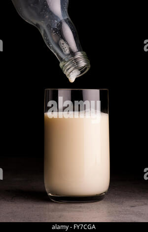 Soja-Milch aus der Flasche in ein Glas gegossen wird. Schwarzer Hintergrund. Stockfoto