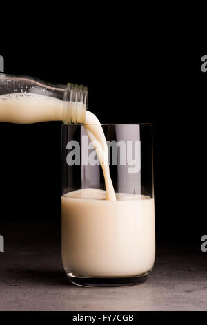 Soja-Milch aus der Flasche in ein Glas gegossen wird. Schwarzer Hintergrund. Stockfoto