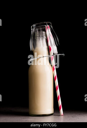 Soja-Milch in Glasflasche und gestreiften Trinkhalm. Schwarzer Hintergrund. Stockfoto