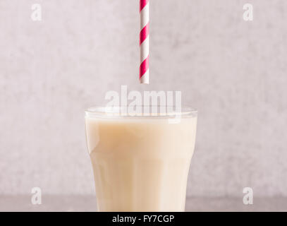 Hafermilch in ein Glas mit gestreiften Trinkhalm oben. Stein Wand Hintergrund. Stockfoto