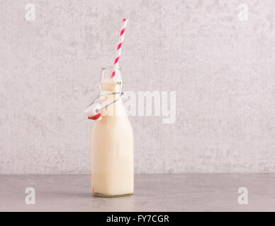 Hafermilch in einer Glasflasche mit gestreiften trinken Stroh am Küchentisch. Hintergrund mit textfreiraum Steinmauer. Stockfoto