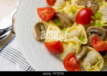 Hausgemachte Tortellini gefüllt mit Pilzen und Frühlingszwiebeln, mit Cherry-Tomaten Stockfoto