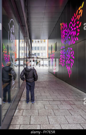 Älterer Mann zu Fuß durch Einkaufszentrum Passage mit bunten blattförmigen Lichter auf schwarze Wand, Stuttgart, Deutschland Stockfoto