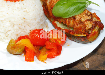 Gefüllte Zucchini, Reis, geschmorte Paprika und Tomaten, Gemüse, Beilagen, garniert mit Basilikum-Blätter auf einer Platte Stockfoto