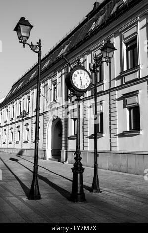 Schwarz / weiß Foto einer Vintage Schmiedeeisen Uhr zwischen zwei Straßenlaternen angebracht. Stockfoto