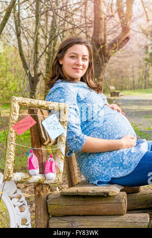 Schöne lächelnd schwangere Frau outdoor im Park auf der Bank. Stockfoto