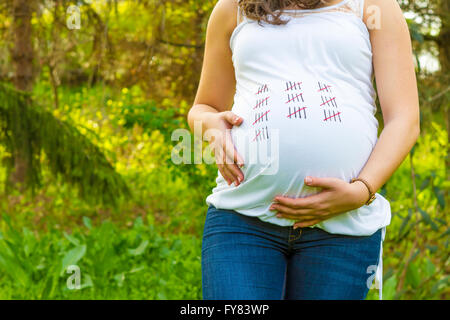 Schwangere junge Frau im Freien bei warmen Sommertag hautnah mit dem Kalender auf ihr T-shirt. Stockfoto