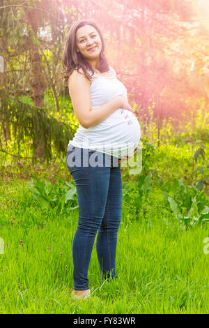 Porträt von glücklichen schwangeren jungen Frau lächelnd im Freien in warmen Sommertag. Stockfoto