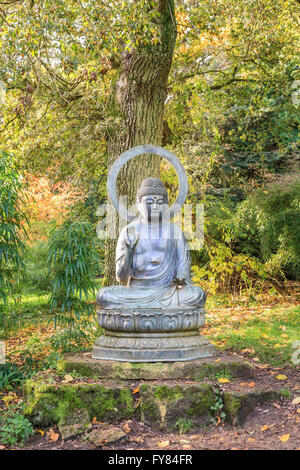 Buddha-Statue sitzt unter einem Baum im zündeten Arboretum, zündeten, Moreton-in-Marsh, Gloucestershire Stockfoto