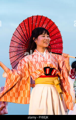 Yosakoi hinokuni Dance Festival, lächelnde Frau in Yukata Jacke, Tanzen mit roten Sonnenschirm über ihre Schulter, am frühen Abend, in Kumamoto, Japan. Stockfoto