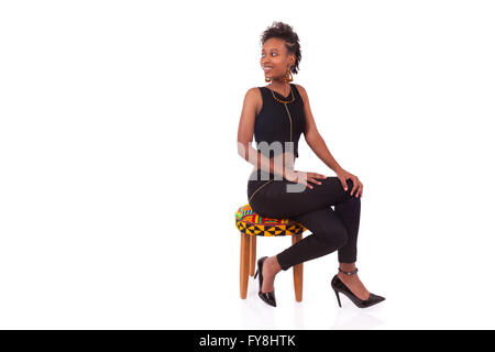 Schöne afrikanische amerikanische Frau sitzt auf einem Hocker isoliert auf weißem Hintergrund Stockfoto