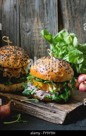 Zwei hausgemachte Veggie-Burger mit Süßkartoffel, frische Radieschen und Erbsen-Sprossen, serviert auf Schneidbrett aus Holz über hölzerne Hinterg Stockfoto