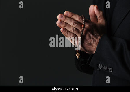 Hände des Priesters holding Rosenkranz und beten auf schwarzem Hintergrund Stockfoto