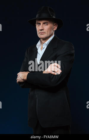 Zuversichtlich Geschäftsmann stehend mit Armen gefaltet auf schwarzem Hintergrund und Blick in die Kamera Stockfoto