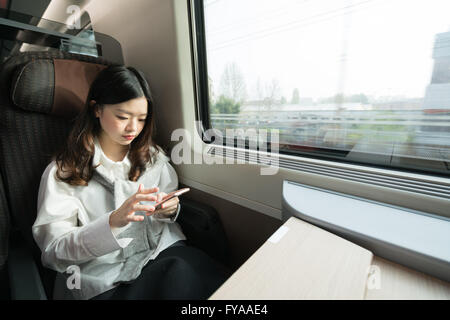 Schöne Asiatin mit Smartphone unterwegs im Zug, Kommunikations-Konzept Stockfoto