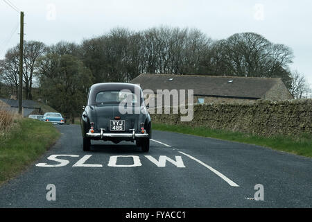 Ein Jahrgang, schwarz, britische Auto fährt auf einer Straße mit dem Wort langsam auf die Straße unten geschrieben. Stockfoto