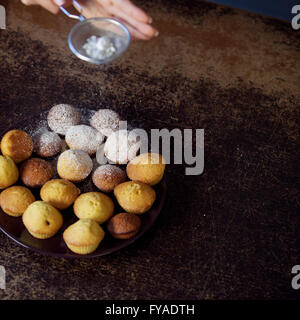 Zarte Frauenhand Beregnung Puderzucker über frische Muffins. Nahaufnahme Stockfoto