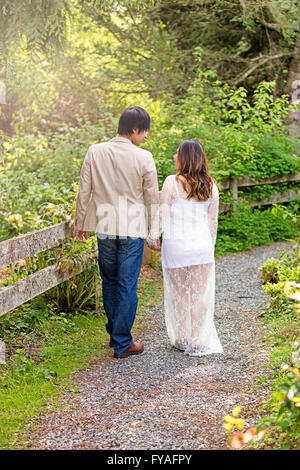 Erwarten, dass Mama und Papa, Rücken zur Kamera, zu Fuß auf den Weg durch den Wald, während Hand in Hand. Stockfoto