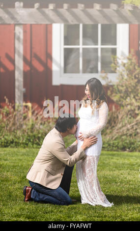 Ehemann küssen Bauch der werdenden Mutter kniend vor ihr auf dem Rasen. Dunst Lichteffekt Bild angewendet. Stockfoto