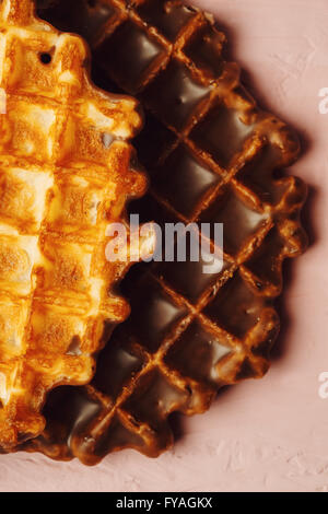 Runde Waffeln mit Schokolade Glasur Extreme Nahaufnahme auf rosa Hintergrund. Eine Waffel mit Puderzucker, eine ohne. Stockfoto