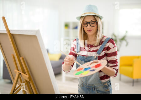 Junge Künstlerin Mischen von Farben auf einer Palette und malen auf eine Leinwand zu Hause Stockfoto