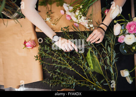 Draufsicht der Hände der jungen Frau Florist schneiden Blumen mit Schere und Gestaltung Bouquet am schwarzen Tisch Stockfoto