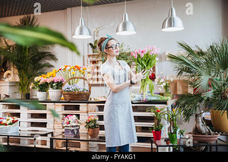 Schöne junge Frau Florist in Gläsern stehen und hält Rosenstrauss rosa Tulpen im Blumenladen Stockfoto