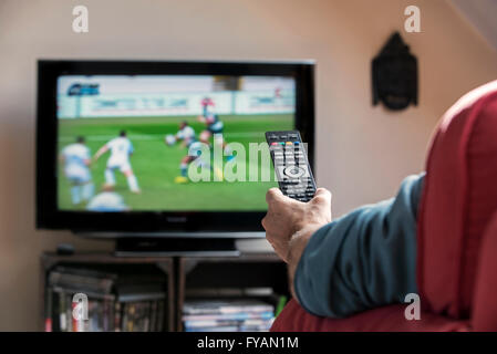 Mann in bequemen Stuhl Schaltkanäle mit Fernbedienung erfreulich Programm am Fernseher im Wohnzimmer suchen Stockfoto