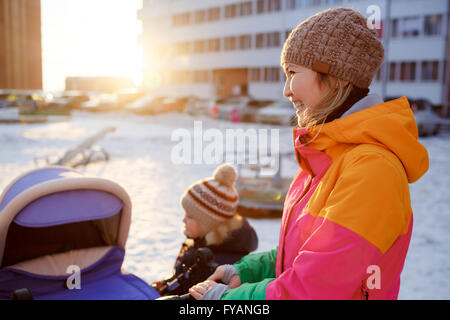 Junge Mutter mit Kind Kinderwagen im Winter bei Sonnenuntergang wandern. Stockfoto