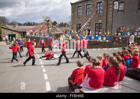 Kinder tanzen um Maypole in Wray, Lancashire, Großbritannien. April 2016. Schüler der Wray-Stiftungsgrundschule feiern die Eröffnung des Wray Vogelscheuche-Festivals, indem sie im Kreis um den Maibaum tanzen. Stockfoto