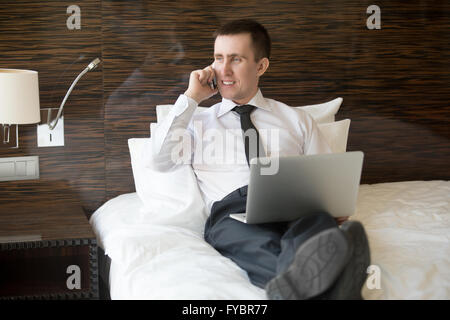 Lächelnd junges Unternehmen attraktive Mann sitzen mit Laptop und Herstellung. Geschäftsmann, arbeiten von zu Hause oder in Reise Stockfoto