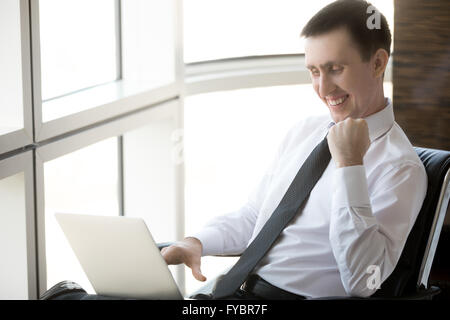 Porträt von fröhlich hübscher junger Geschäftsmann sitzt in seinem Büro mit Technik. Glückliche Unternehmen Unternehmer Stockfoto