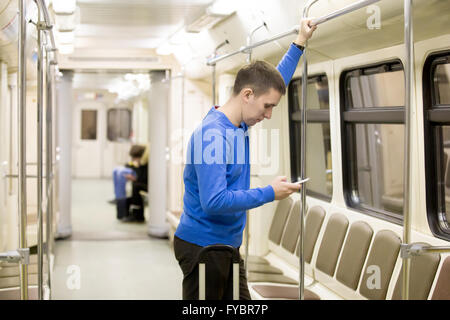 Seite Ansicht Porträt der schönen jungen Mann casual-Style Kleidung stehen in der u-Bahn mit smartphone Stockfoto