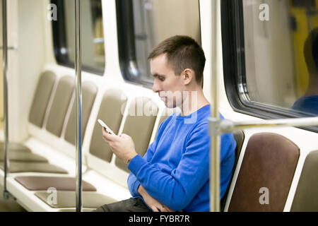 Porträt von schönen jungen Mann casual-Style Kleidung sitzt auf dem Stuhl in der u-Bahn mit Smartphone. PKW Stockfoto